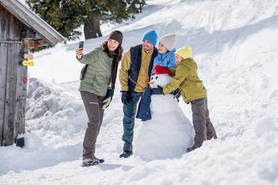 Zwei Erwachsene und zwei Kinder die ein Selfie mit deren Schneemann machen. | © Ski Juwel Alpbachtal Wildschönau | Christoph Oberschneider
